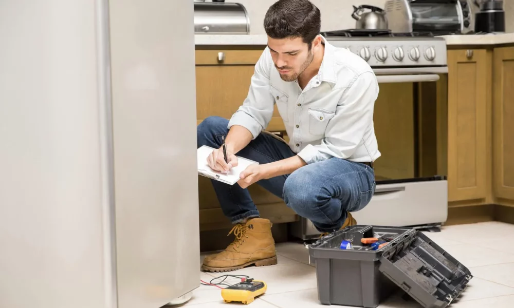 portrait-handsome-male-technician-doing-work-report-broken-fridge-home-kitchen